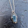 Coffin shaped green moss agate on a chain resting on a black surface