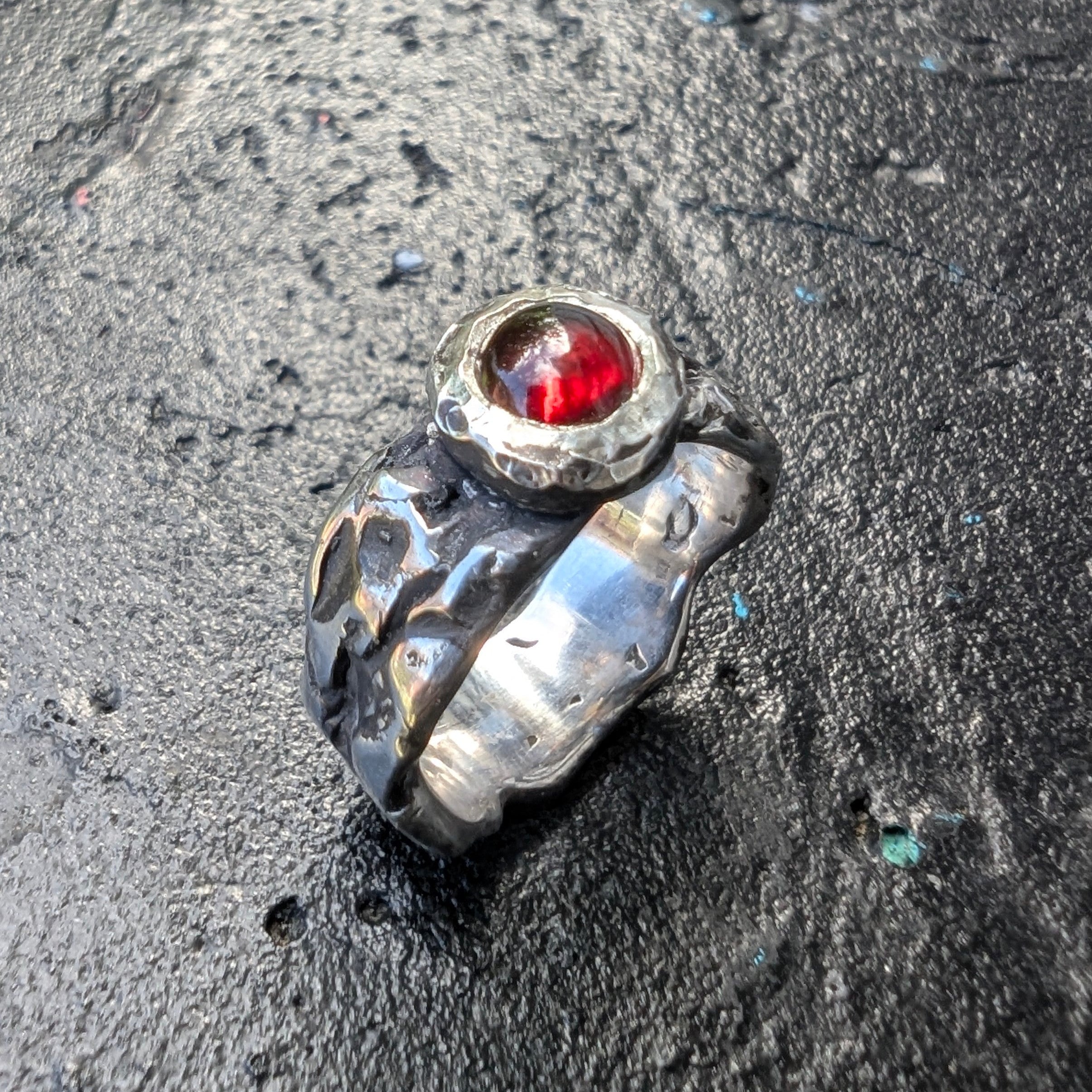 Silver ring with a red gemstone on a dark textured surface